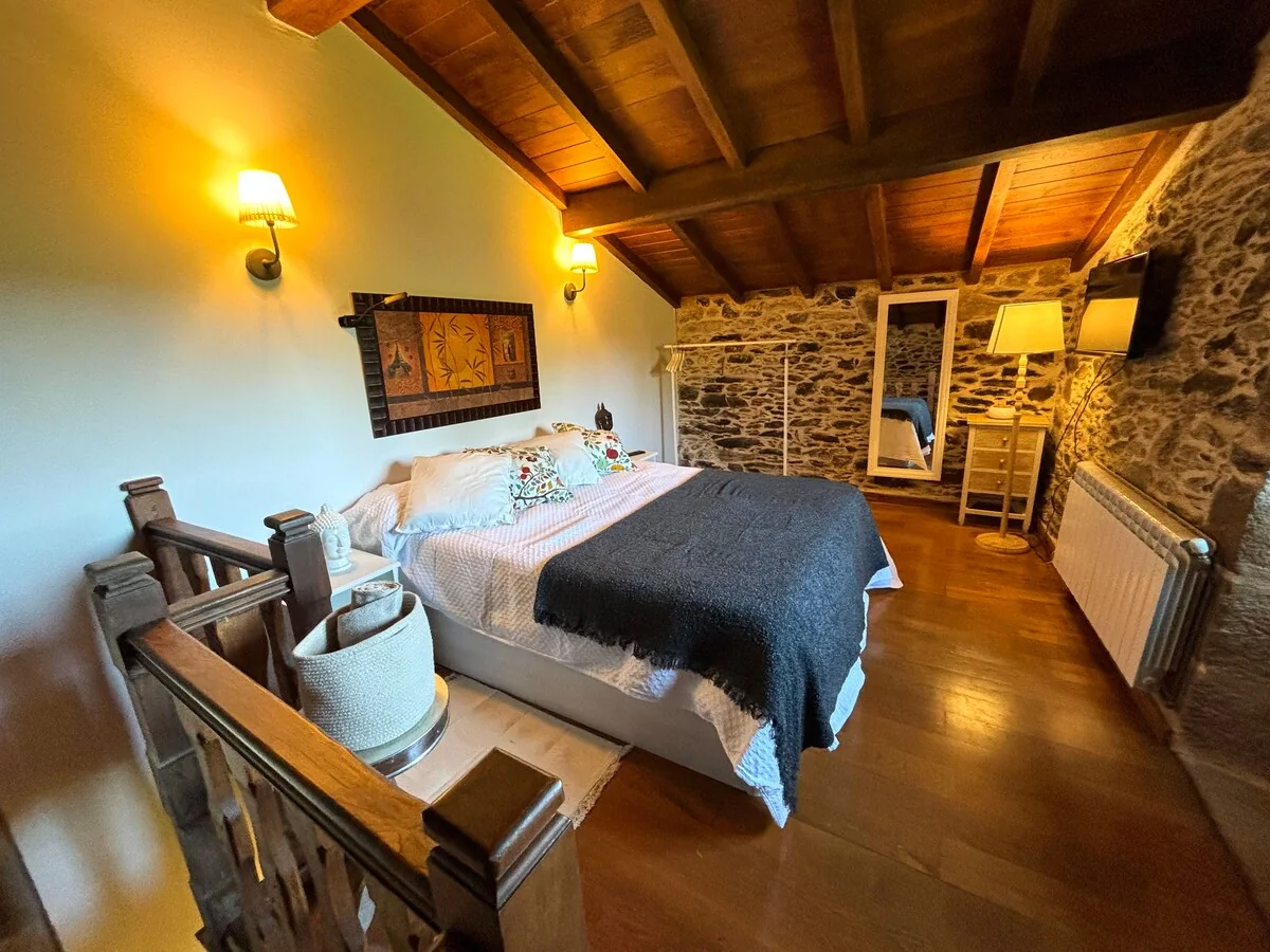 Dormitorio abuhardillado del apartamento F. de Castro, con cama de matrimonio bajo las vigas
